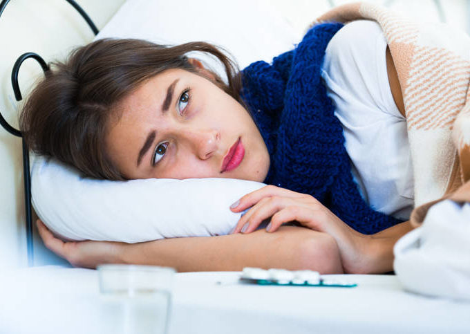 A young woman laying her head a white pillow with a blue scarf.