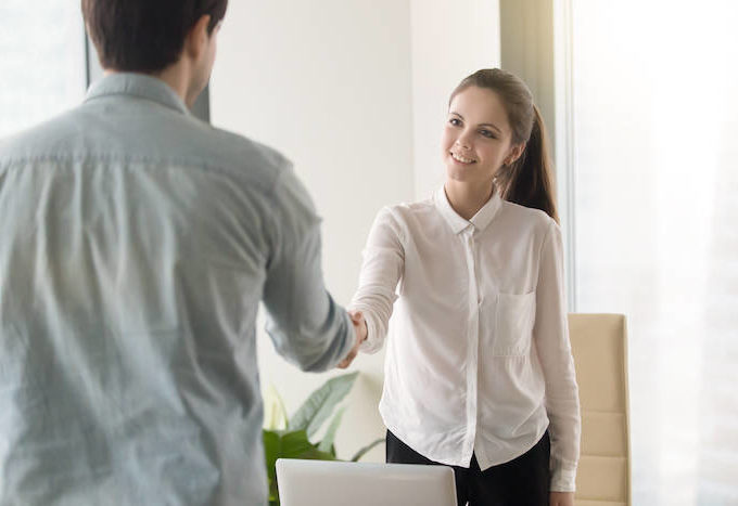 Woman dressed in a white button down shirt shaking hands across the table.