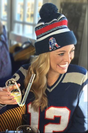 A woman dressed in a patriots jersey smiling.